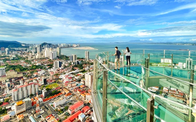 Couple enjoying the view from The Top, Penang's glass skywalk overlooking the city and sea.