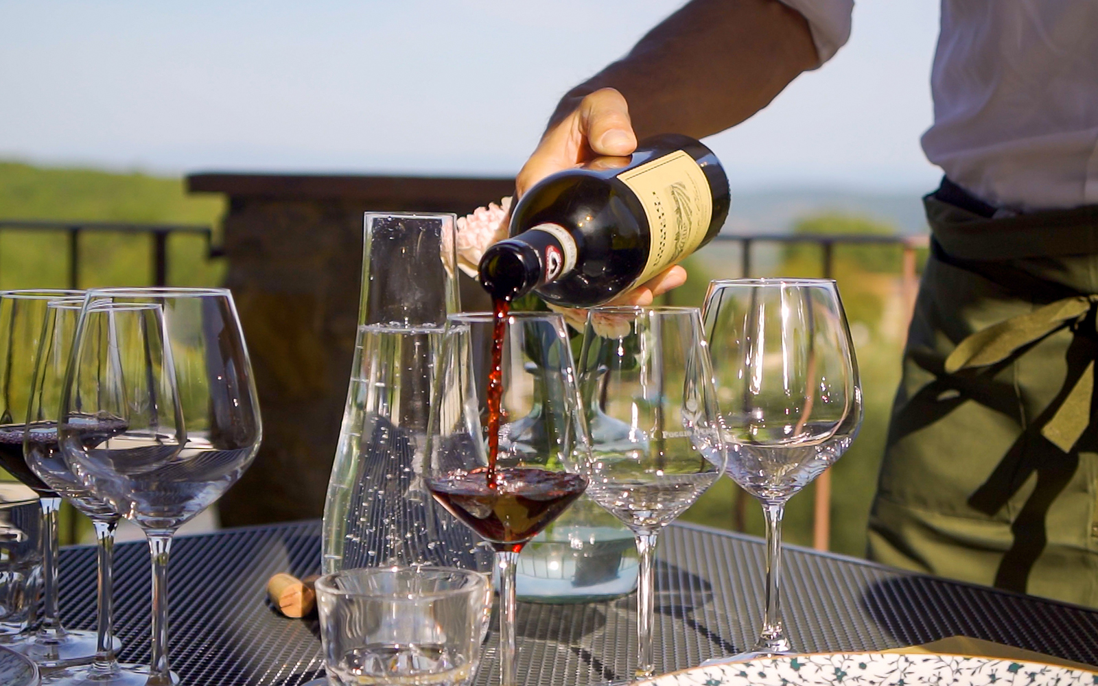 Wine being poured into glasses on a patio with a scenic view.