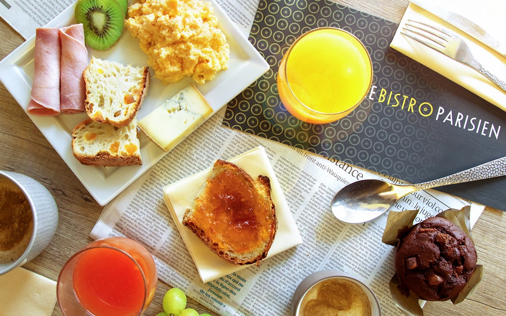Le Bistro Parisien breakfast spread with ham, cheese, bread, scrambled eggs, and juice.