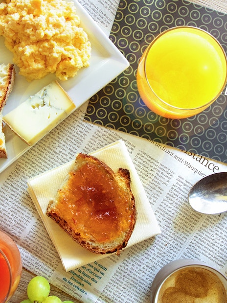 Le Bistro Parisien breakfast spread with ham, cheese, bread, scrambled eggs, and juice.