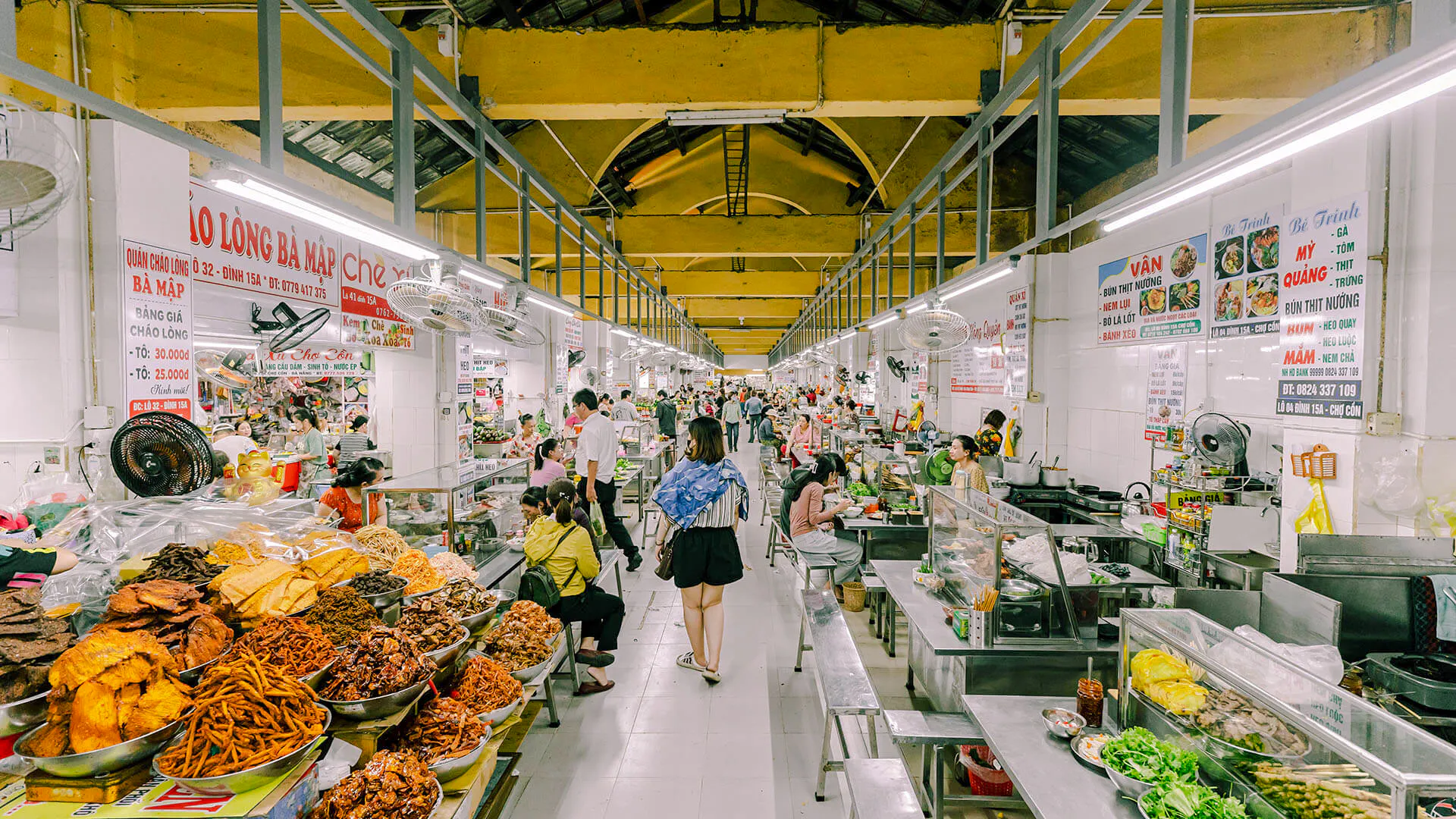 Da Nang market with food stalls and people enjoying breakfast during a guided city tour.