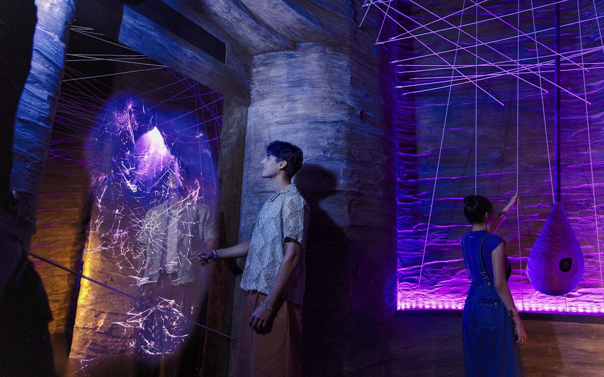 Visitors exploring cave spider exhibit at Exploria, Mandai Wildlife, with interactive web display.