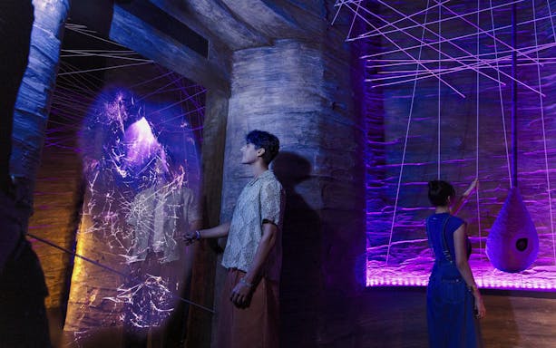 Visitors exploring cave spider exhibit at Exploria, Mandai Wildlife, with interactive web display.