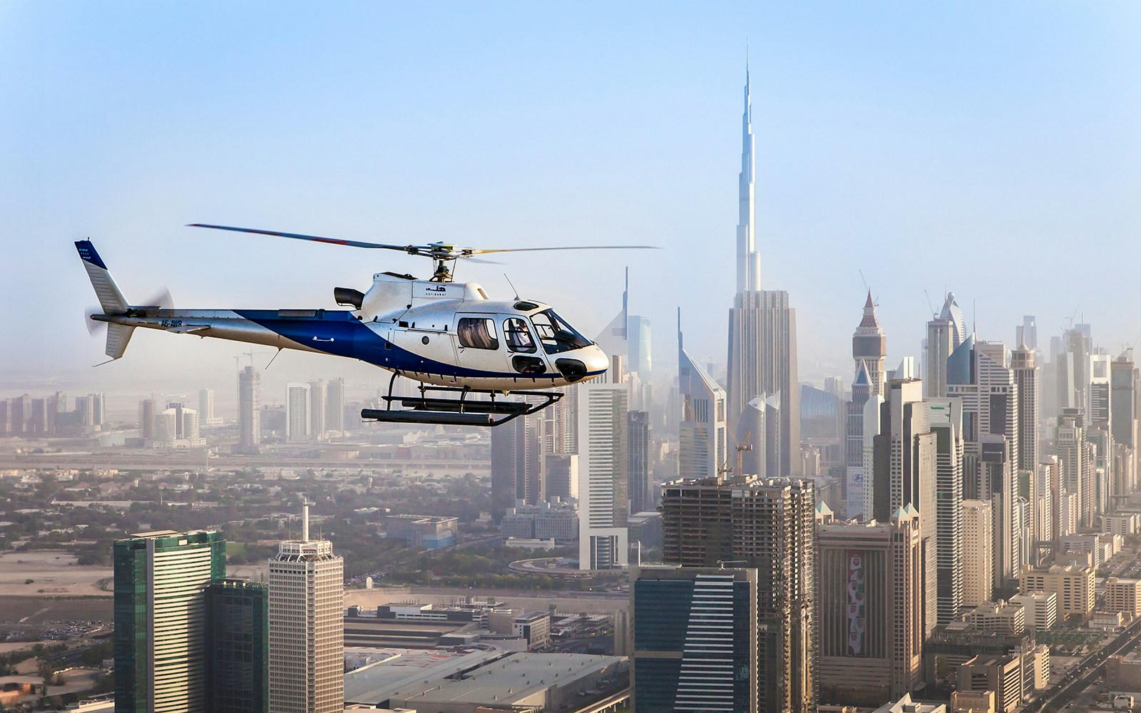 Helicopter flying over Dubai skyline with Burj Khalifa in the background.