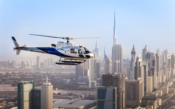 Helicopter flying over Dubai skyline with Burj Khalifa in the background.
