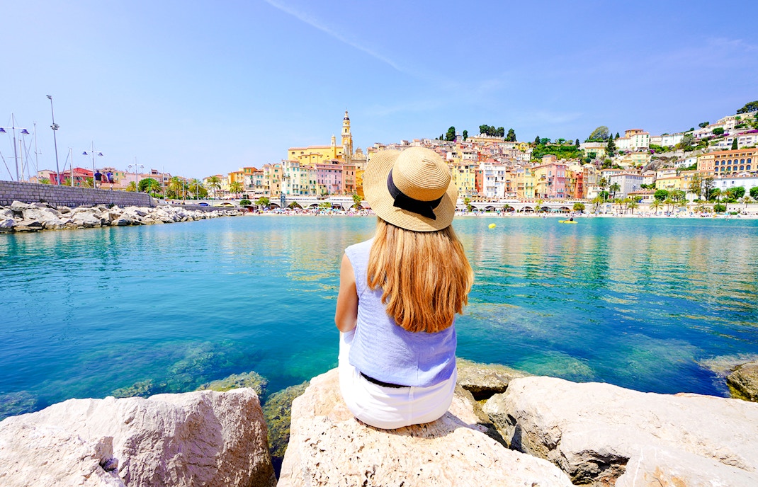 Woman sitting on rocks overlooking colorful buildings in Nice, France.