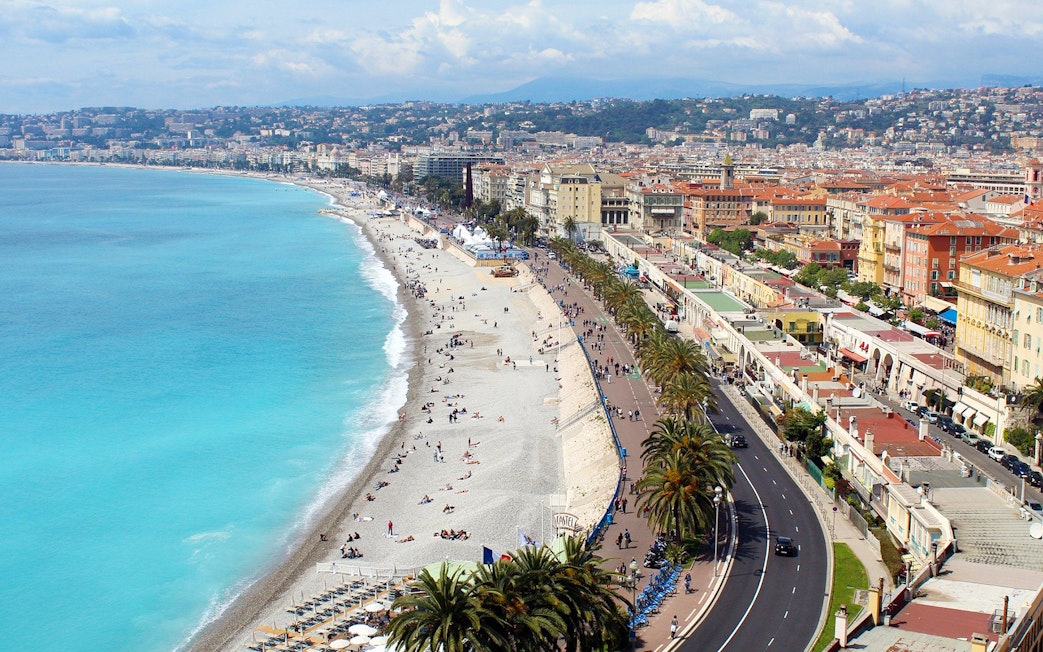 Promenade des Anglais in Nice with beachgoers and coastal view.