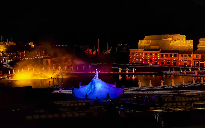 Performer in blue dress at Hoi An Memories show with illuminated backdrop.