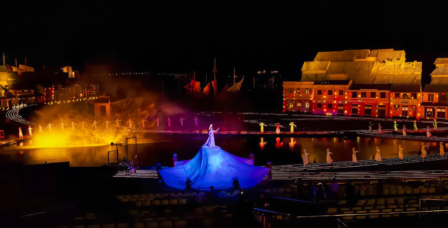 Performer in blue dress at Hoi An Memories show with illuminated backdrop.