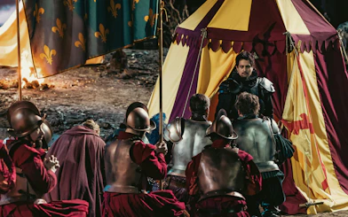 Knights kneeling before a tent with a man in armor, depicting a historical scene related to Willem van Oranje.