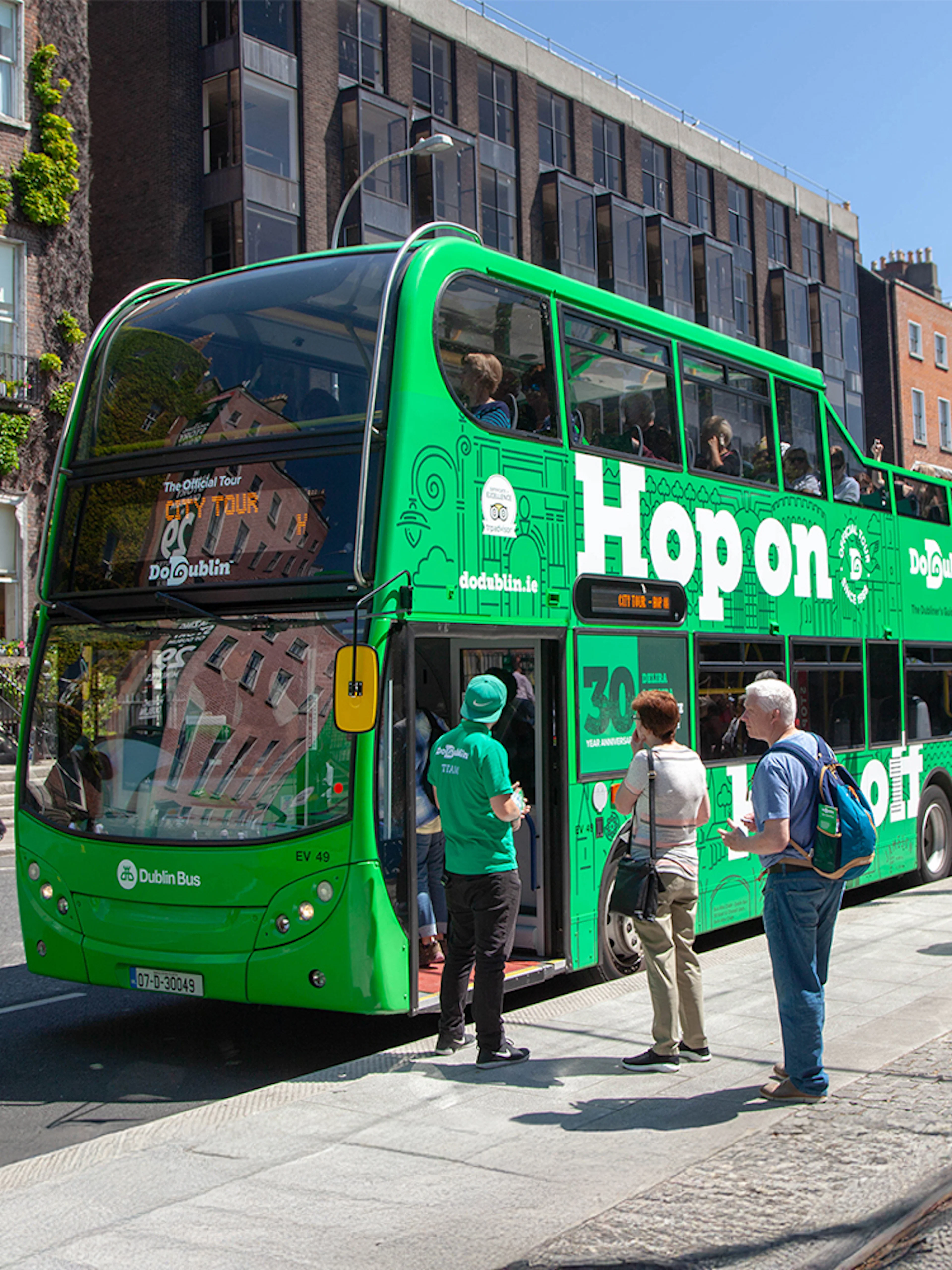 Tourists boarding a green Hop on Hop off bus in Dublin city center.