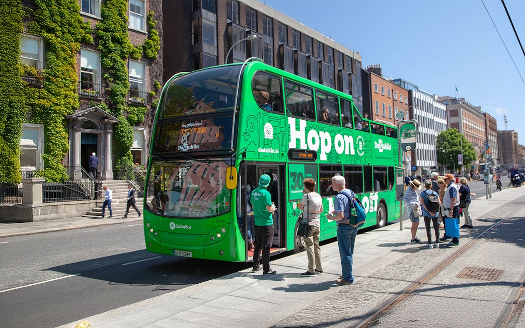 Tourists boarding a green Hop on Hop off bus in Dublin city center.