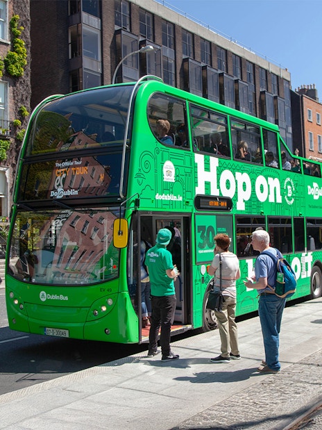 Tourists boarding a green Hop on Hop off bus in Dublin city center.