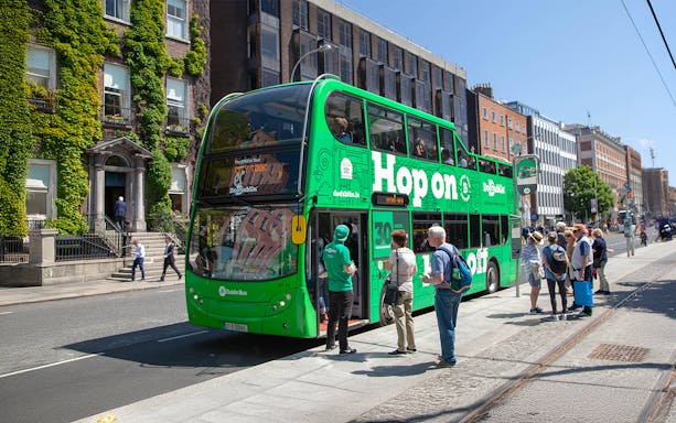 Tourists boarding a green Hop on Hop off bus in Dublin city center.