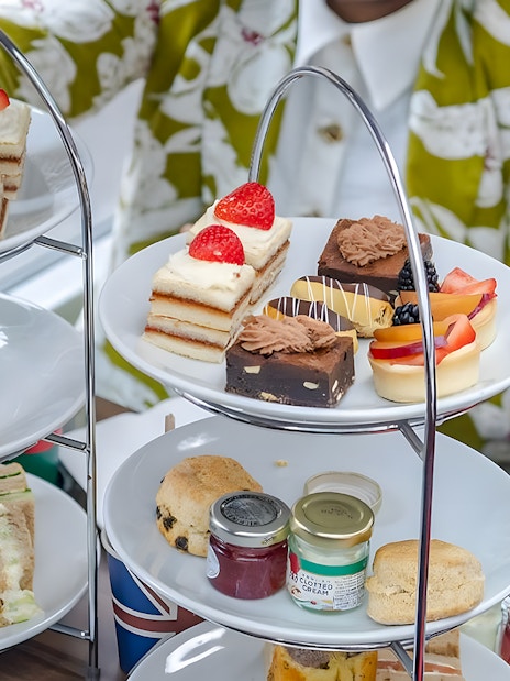 Afternoon tea pastries and sandwiches on a tiered stand during a London sightseeing bus tour.