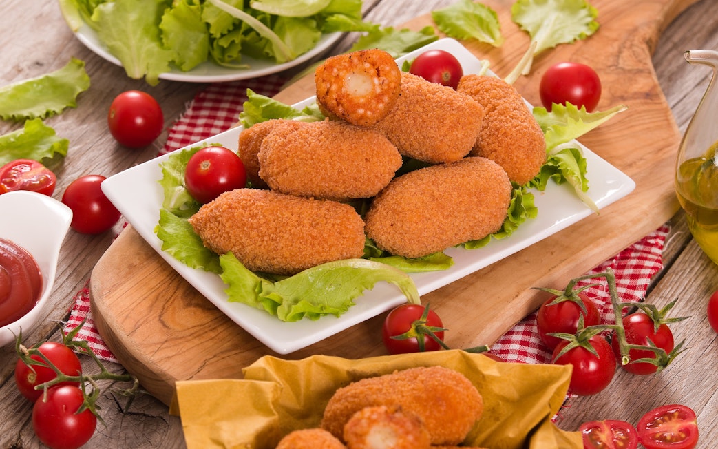 Suppli on a plate with lettuce and cherry tomatoes, Italian appetizer.