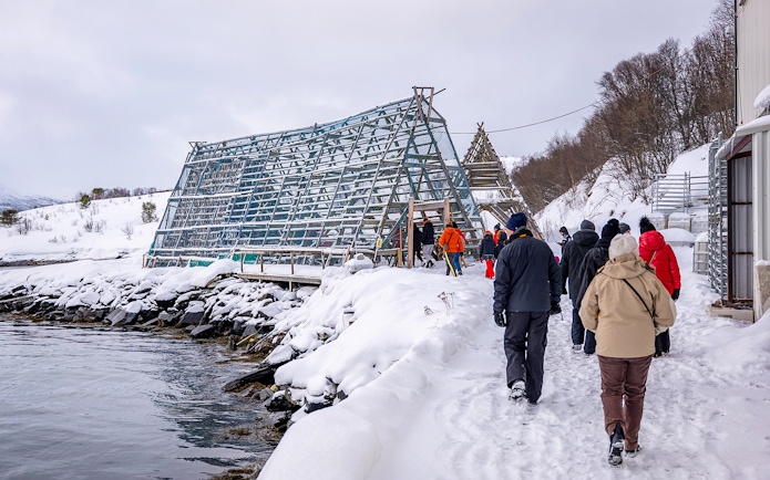 Tourists walking by a traditional fish drying rack in snowy Tromso during Arctic Fjord Cruise.