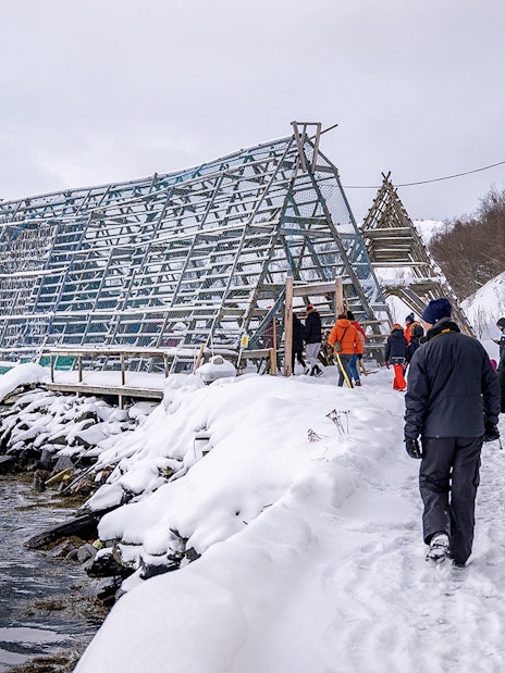Tourists walking by a traditional fish drying rack in snowy Tromso during Arctic Fjord Cruise.