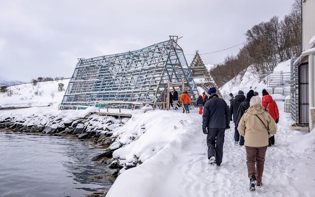 Tourists walking by a traditional fish drying rack in snowy Tromso during Arctic Fjord Cruise.