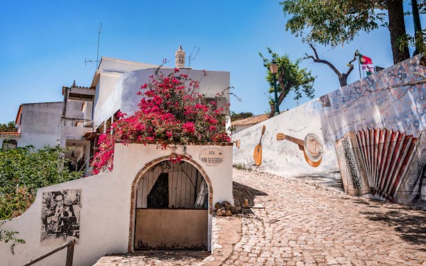 Cobbled street in Albufeira with mural art and vibrant flowers on a Full-Day Quad Tour of Algarve.