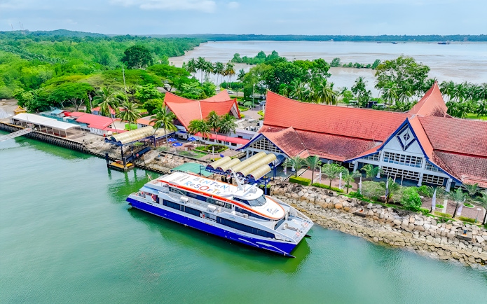 Ferry docked at Bintan Resorts terminal with lush greenery and red-roofed buildings in the background.