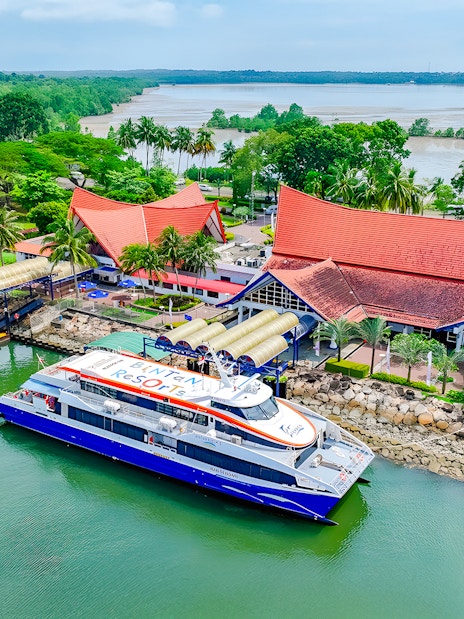 Ferry docked at Bintan Resorts terminal with lush greenery and red-roofed buildings in the background.