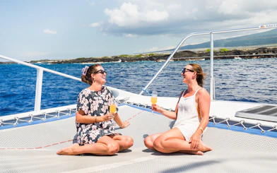 Two women enjoying drinks on a catamaran cruise in Kona, Hawaii.