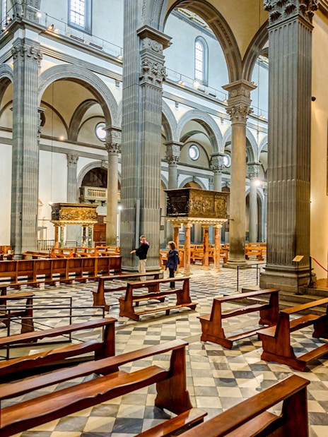 Interior of Basilica di San Lorenzo, Florence, showing columns, pews, and religious artwork.