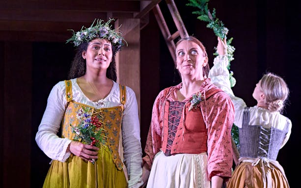 Women in period costumes holding flowers during a performance of "Hamnet.