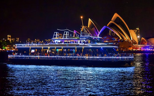 Cruise ship on Sydney Harbour at night with Sydney Opera House in the background.