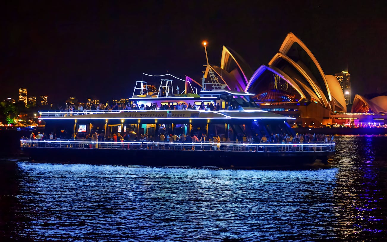 Cruise ship on Sydney Harbour at night with Sydney Opera House in the background.