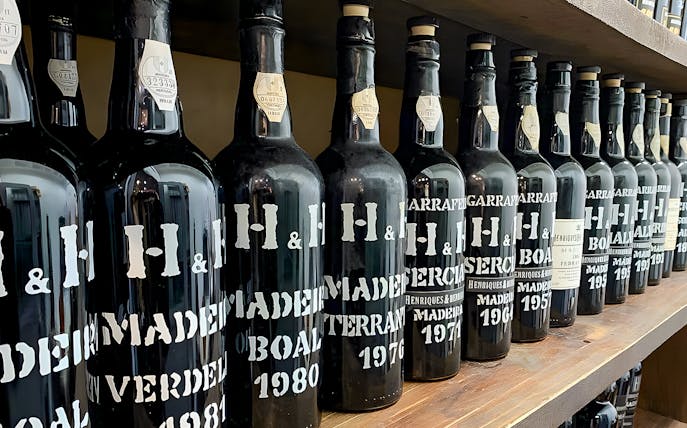 H&H wine bottles on a wooden shelf, showcasing vintage selections for Wine Wanderlust tour.