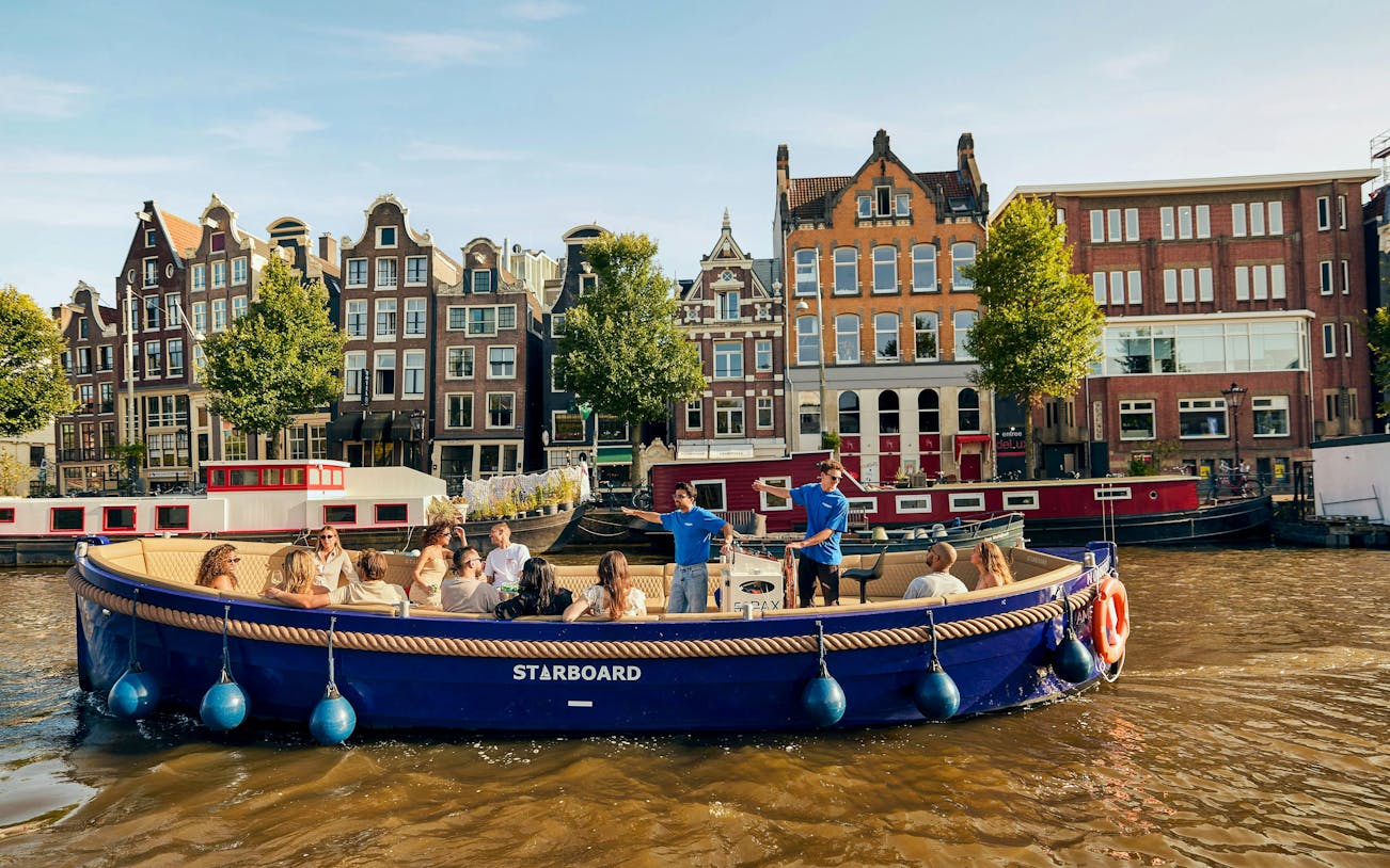 Guests enjoying a canal booze cruise in Amsterdam with historic buildings in the background.