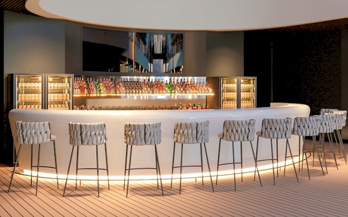 Curved bar counter with stools and illuminated shelves displaying bottles.