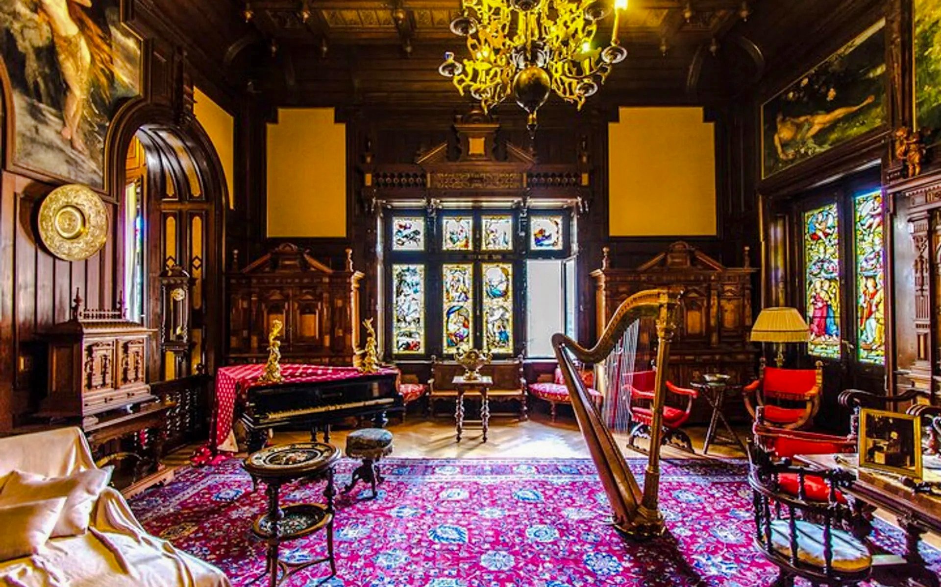 Interior of Peles Castle in Romania featuring ornate woodwork, stained glass, and a harp.