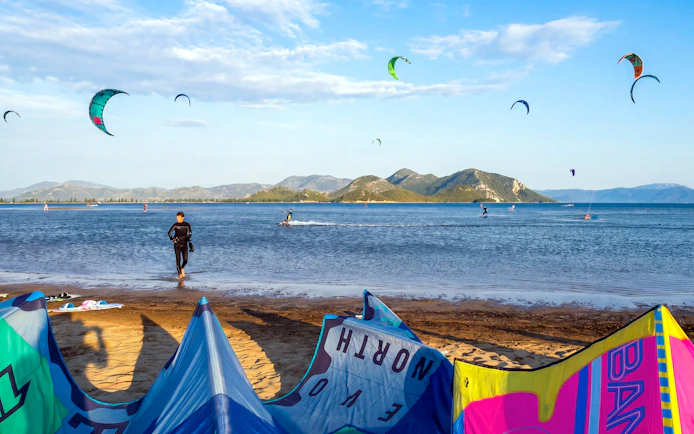 Kiteboarders on the water at Delta Neretva, Croatia with colorful kites in the sky.