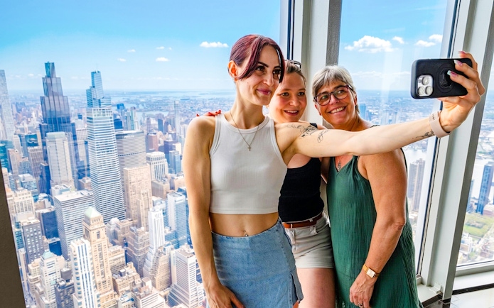 Visitors taking a selfie with New York City skyline from Empire State Building observatory.