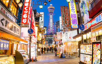 Bustling Osaka street with Tsutenkaku Tower, vibrant signs, and people exploring shops.