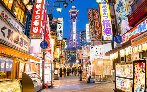 Bustling Osaka street with Tsutenkaku Tower, vibrant signs, and people exploring shops.