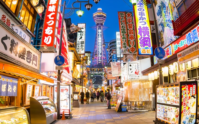 Bustling Osaka street with Tsutenkaku Tower, vibrant signs, and people exploring shops.