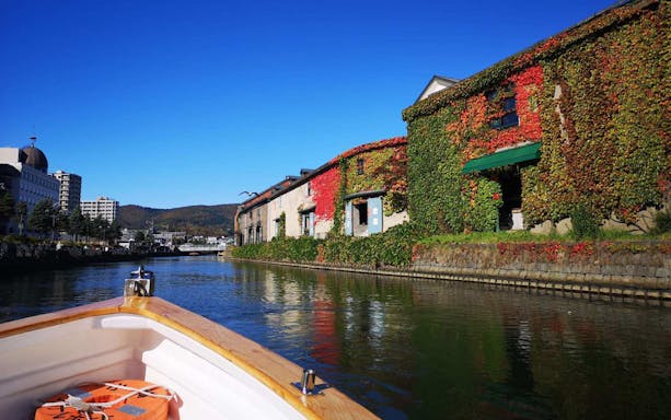 Boat cruising along Otaru Canal with ivy-covered warehouses in Hokkaido, Japan.