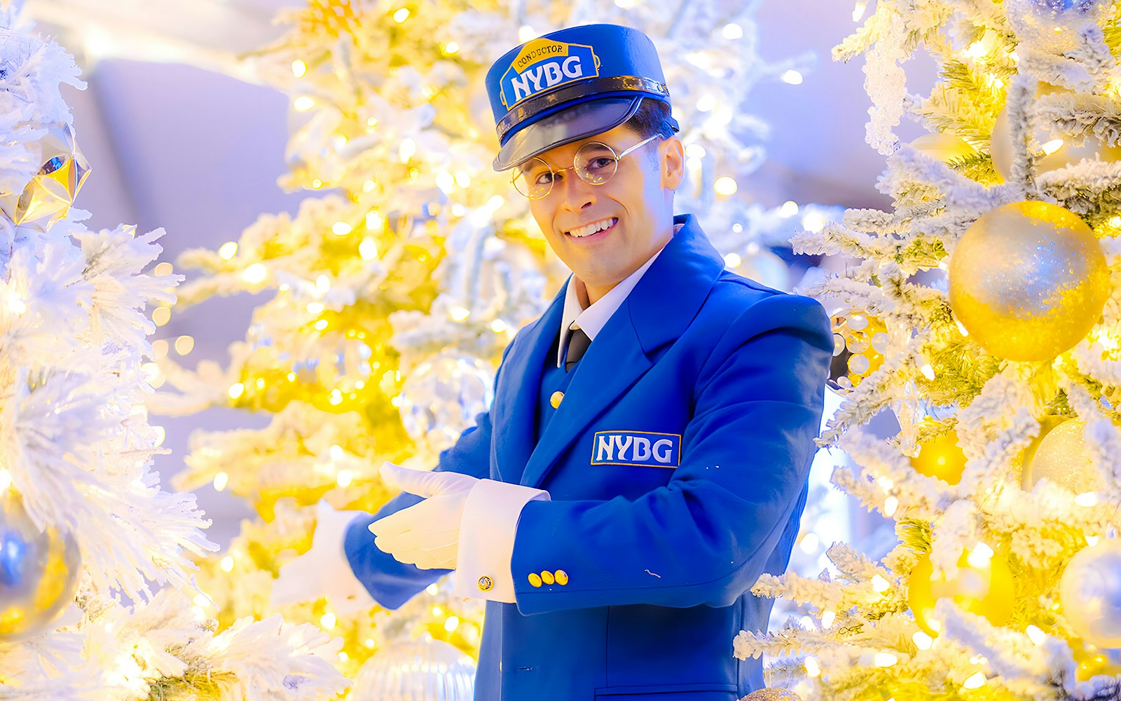 Conductor in blue NYBG uniform amidst festive holiday lights and decorated trees at Holiday Train Show.
