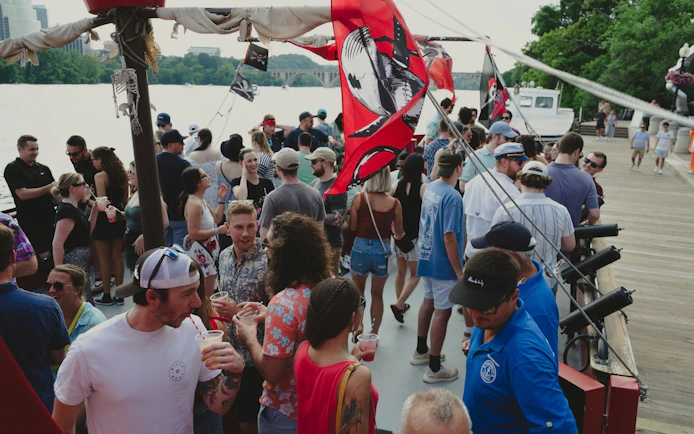 Partygoers on Boomerang Pirate Ship cruise with drinks and DC monuments in background.
