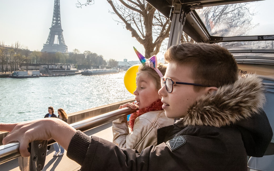 Siblings on Tootbus tour in Paris looking at Seine River with Eiffel Tower in view.