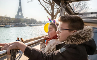 Siblings on Tootbus tour in Paris looking at Seine River with Eiffel Tower in view.