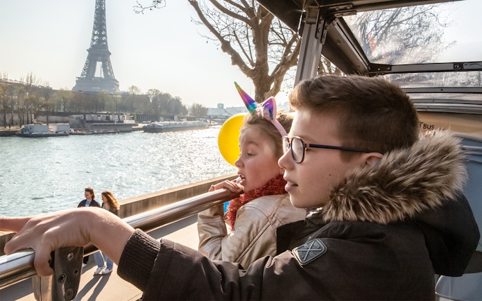 Siblings on Tootbus tour in Paris looking at Seine River with Eiffel Tower in view.