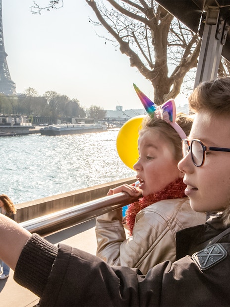 Siblings on Tootbus tour in Paris looking at Seine River with Eiffel Tower in view.