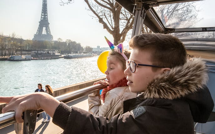 Siblings on Tootbus tour in Paris looking at Seine River with Eiffel Tower in view.