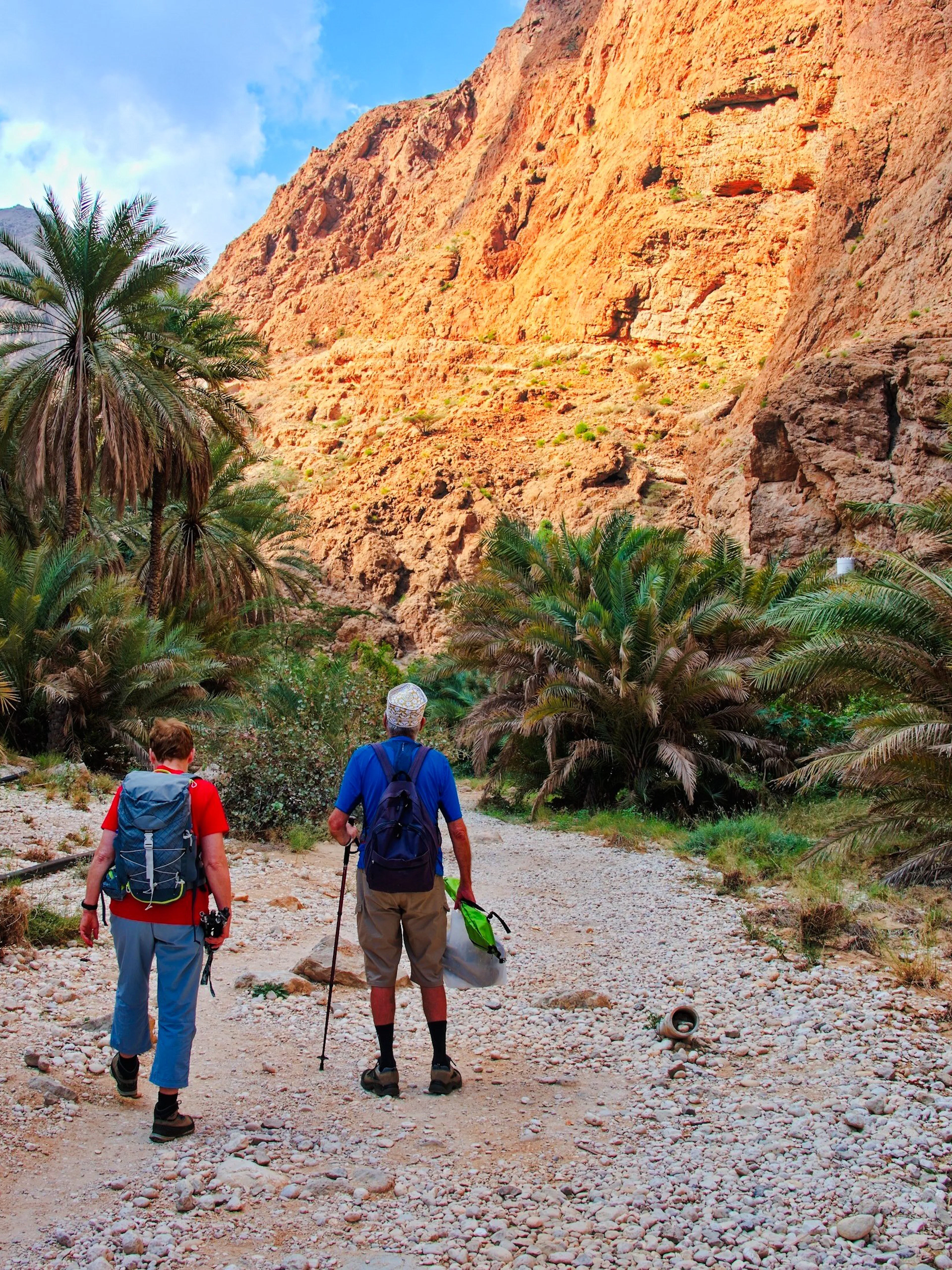 Couple hiking through rocky path surrounded by palm trees in Wadi Shab, Oman.