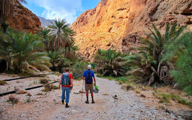 Couple hiking through rocky path surrounded by palm trees in Wadi Shab, Oman.